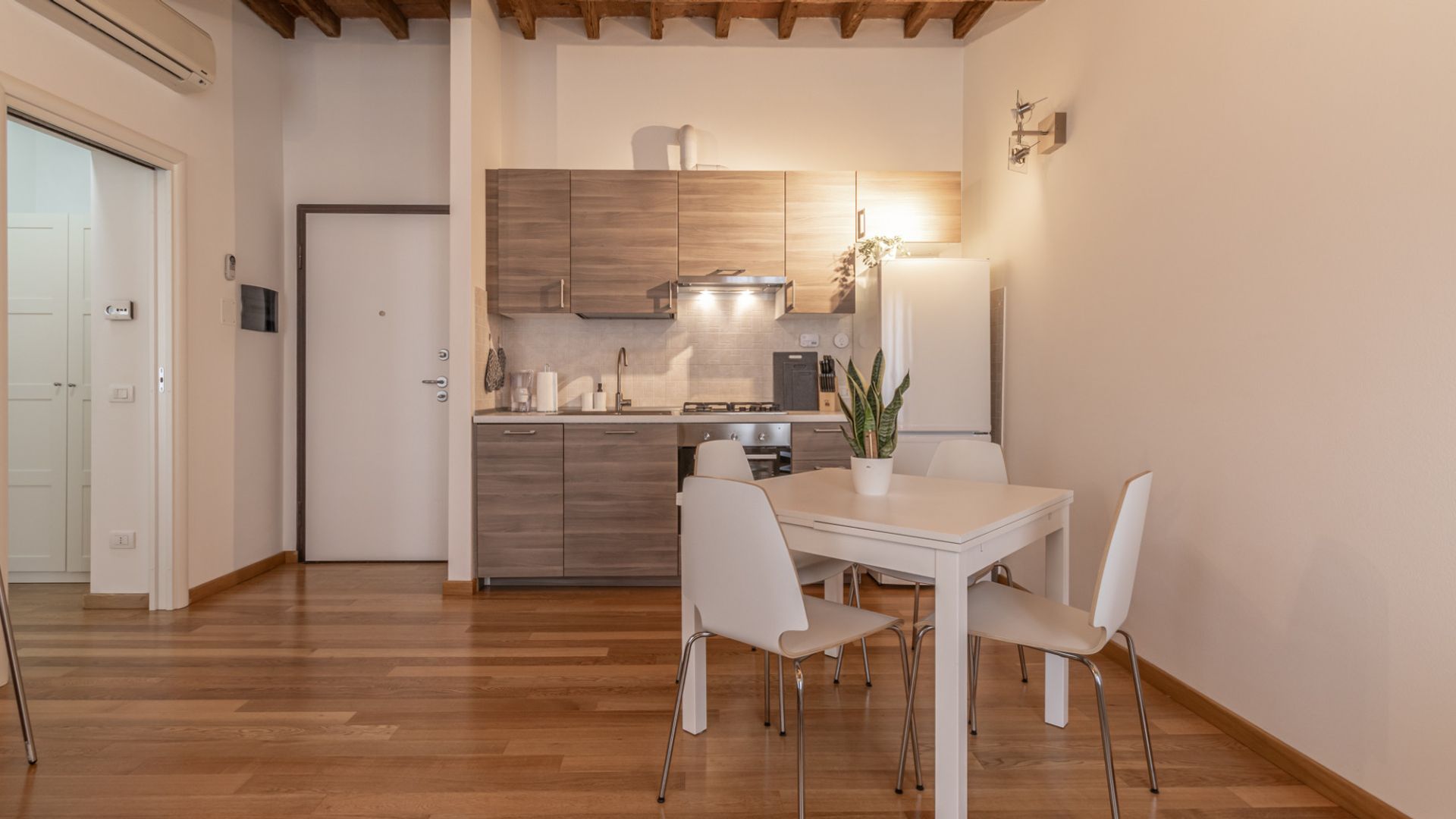 A compact kitchen with wooden cabinets, a white countertop, and a dining area with a white table and chairs.