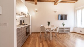 Cocina moderna con armarios de madera, zona de comedor con mesa y sillas, y un televisor de pantalla plana montado en la pared.