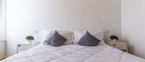 A bed with a white quilted cover, two gray pillows, and two bedside tables with small potted plants.