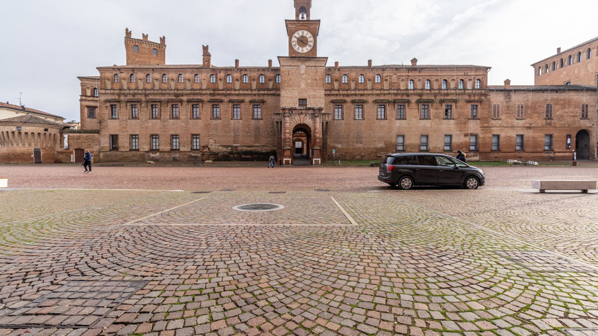 Un edificio histórico con una torre de reloj, un patio empedrado y una entrada pavimentada.
