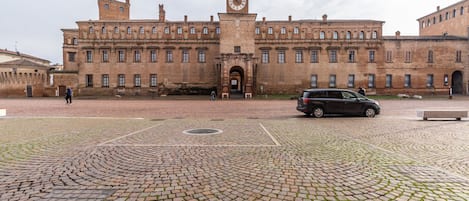 Un edificio histórico con una torre de reloj, un patio empedrado y una entrada pavimentada.
