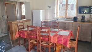 A dining area with a wooden table and chairs, a kitchen with a refrigerator and sink, and a window with blinds.