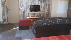 A bedroom with a TV on a wooden stand, a sofa, and a red ottoman.