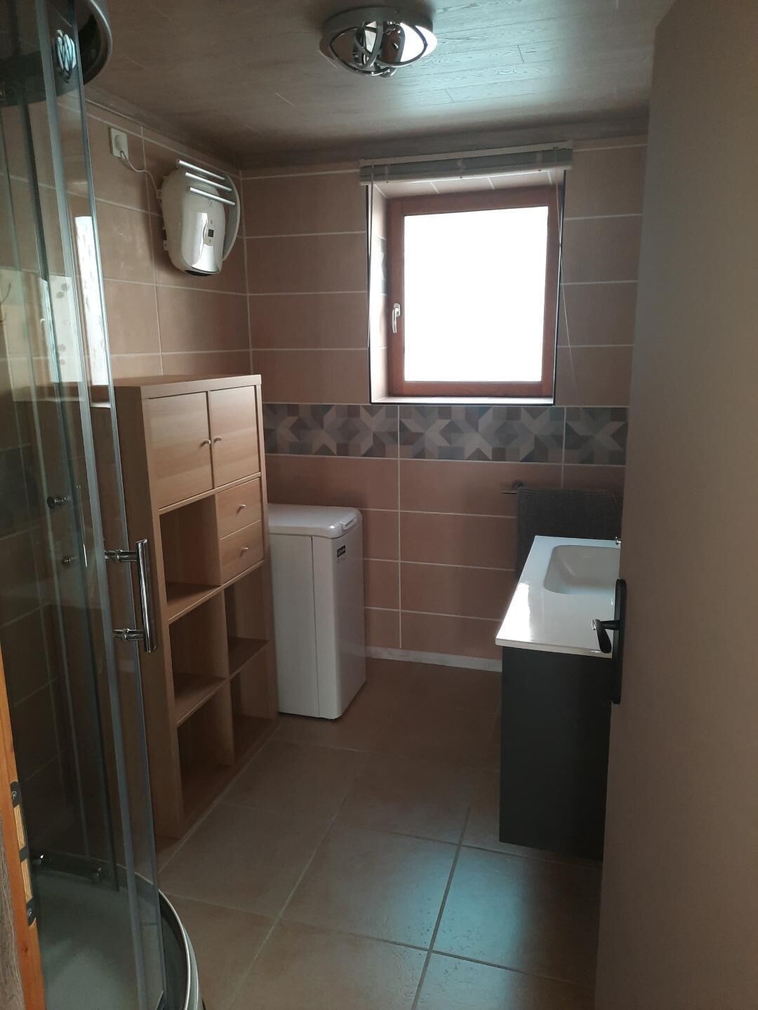 A compact bathroom with a glass shower enclosure, a small white sink, and a window providing natural light.