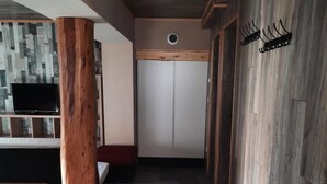A hallway with a wooden floor, a large wooden pillar, a bench, and a TV on a shelf.