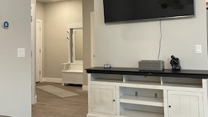 A modern living room with a large flat-screen TV mounted on the wall, a white entertainment unit below, and a wooden floor. - Cute Modern townhouse close many Utah national parks (Cedar City)