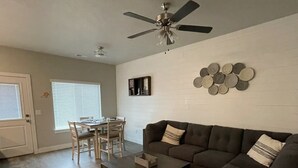 A living room with a dark brown sofa, a coffee table, and a dining area with a table and chairs. - Cute Modern townhouse close many Utah national parks (Cedar City)