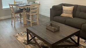 A living room with a dark brown coffee table, a gray sofa, and a dining area with a wooden table and chairs. - Cute Modern townhouse close many Utah national parks (Cedar City)