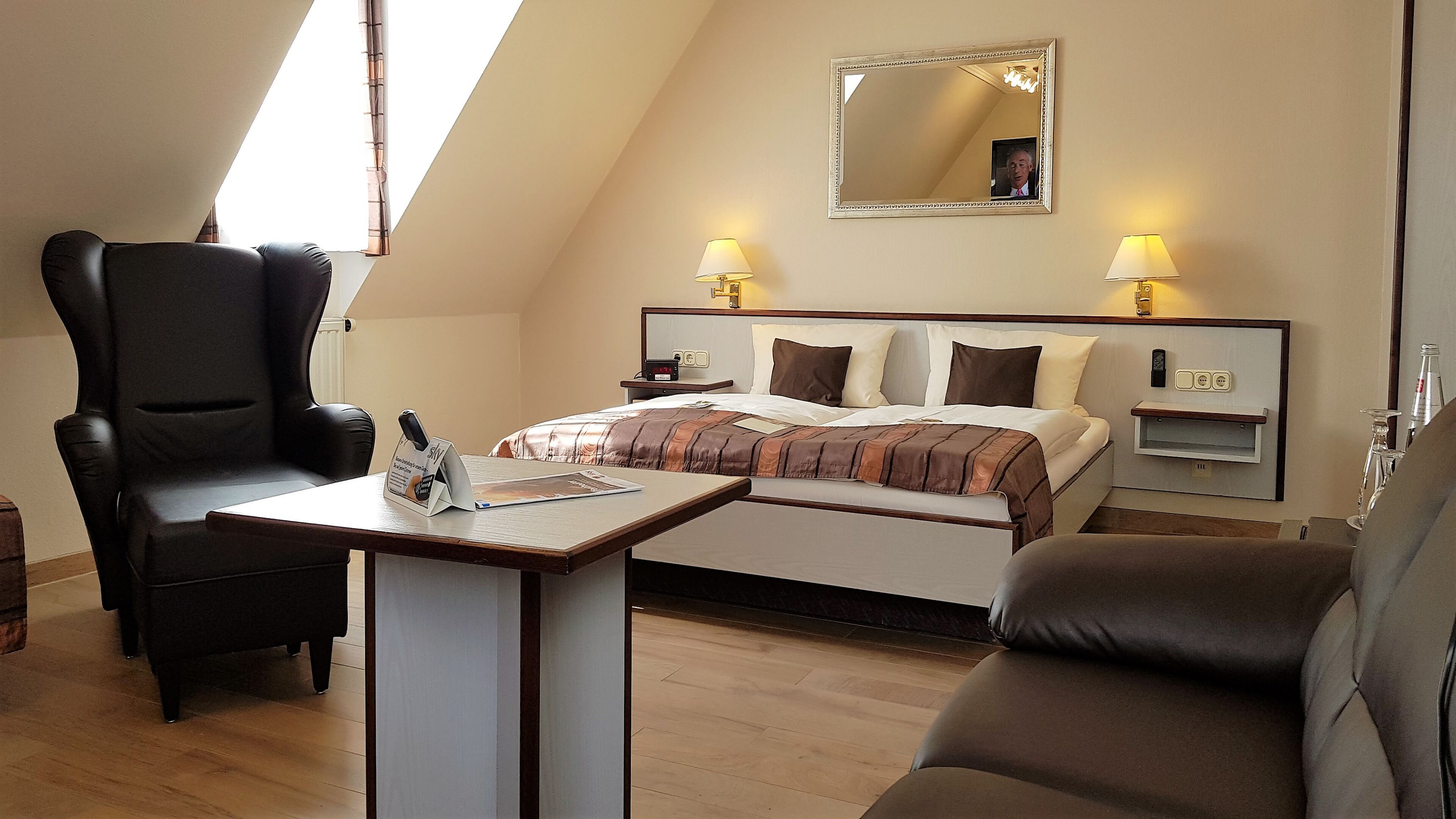 A hotel room with a bed, two bedside tables, a desk, two chairs, a mirror, and a window.