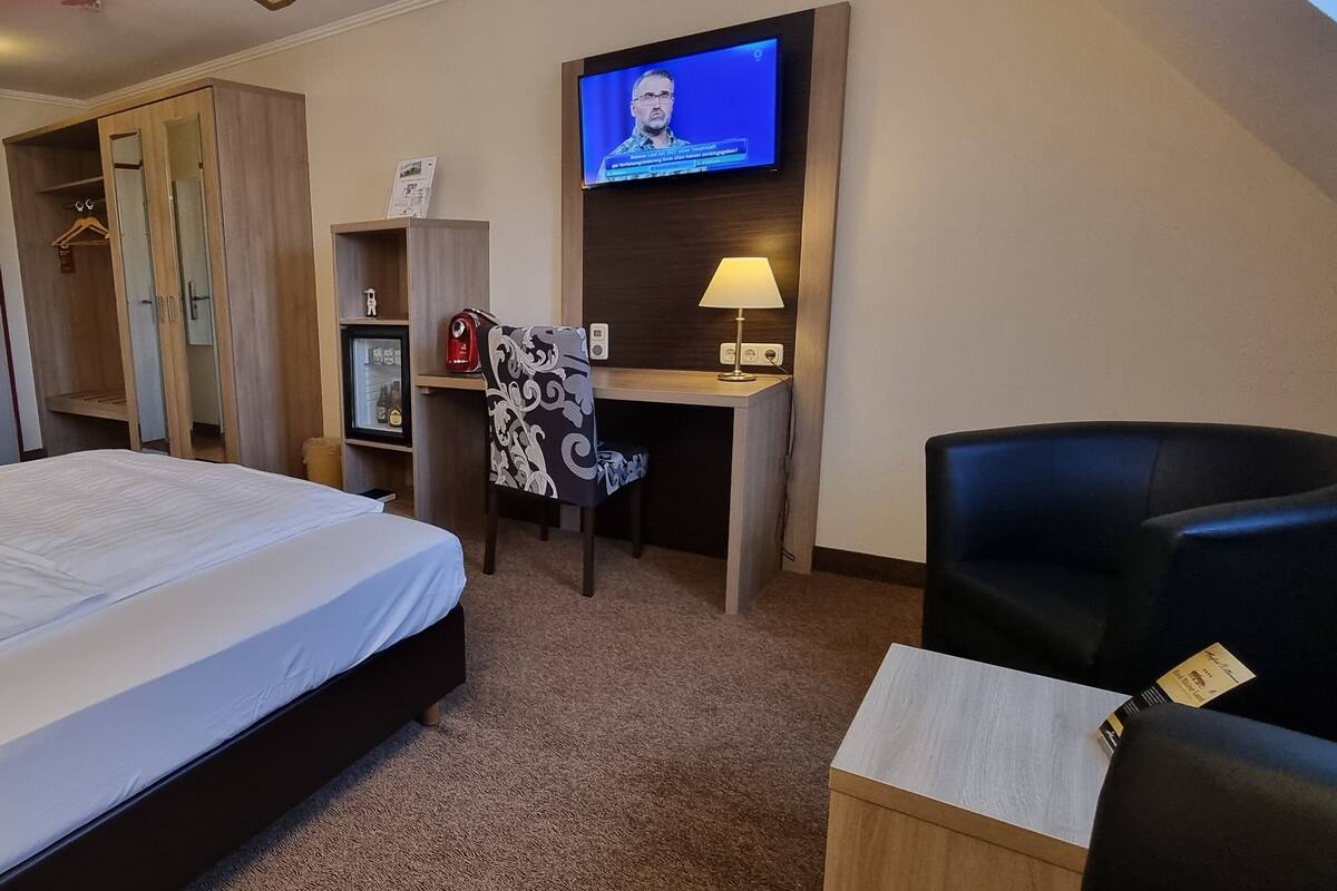 A hotel room with a bed, a desk, a TV, a chair, and a wardrobe.