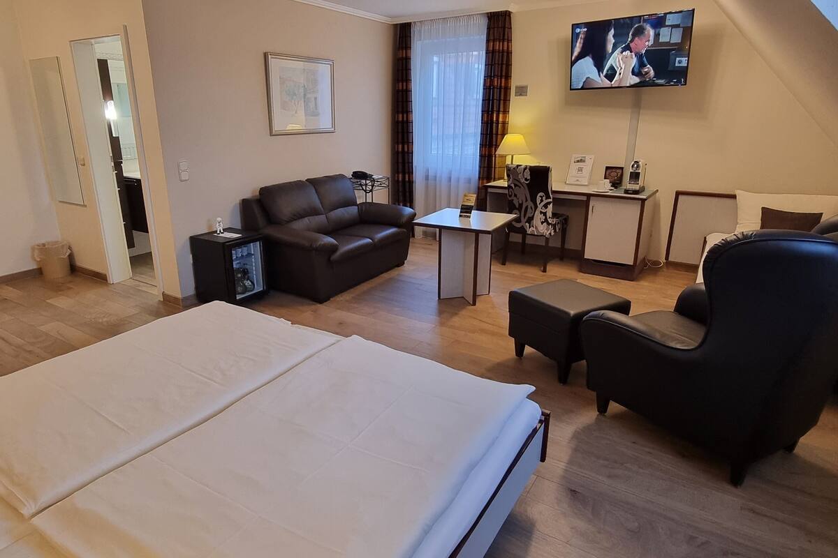 A hotel room with a bed, a sofa, a desk, a chair, and a television.