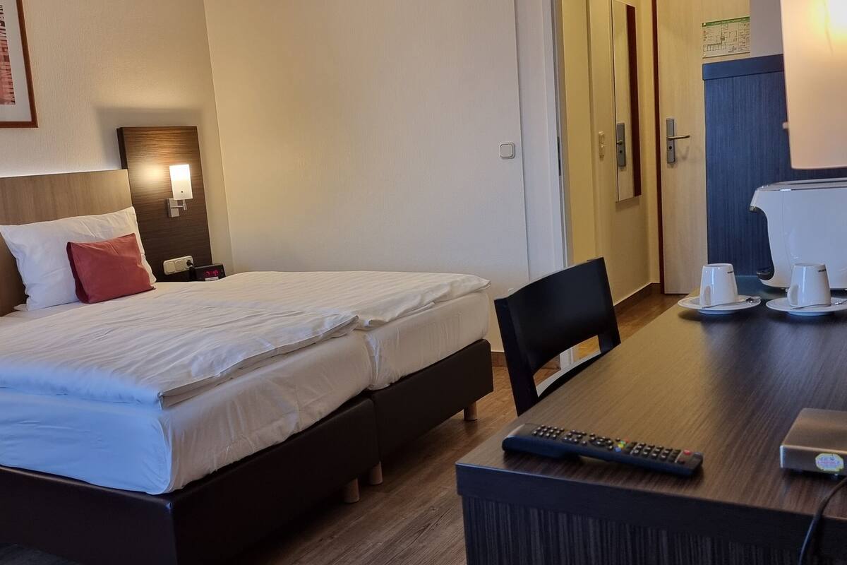 A hotel room with two beds, a desk with a coffee maker, and a TV.