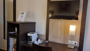 Habitación de hotel con cafetera, refrigerador pequeño, lámpara y un cartel en la pared.