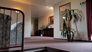 Un vestíbulo de hotel con un espejo grande, una planta en maceta, una silla de madera y suelo alfombrado.