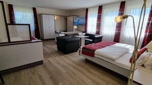 Una habitación de hotel con cama, escritorio, silla, televisor y ventana con cortinas.