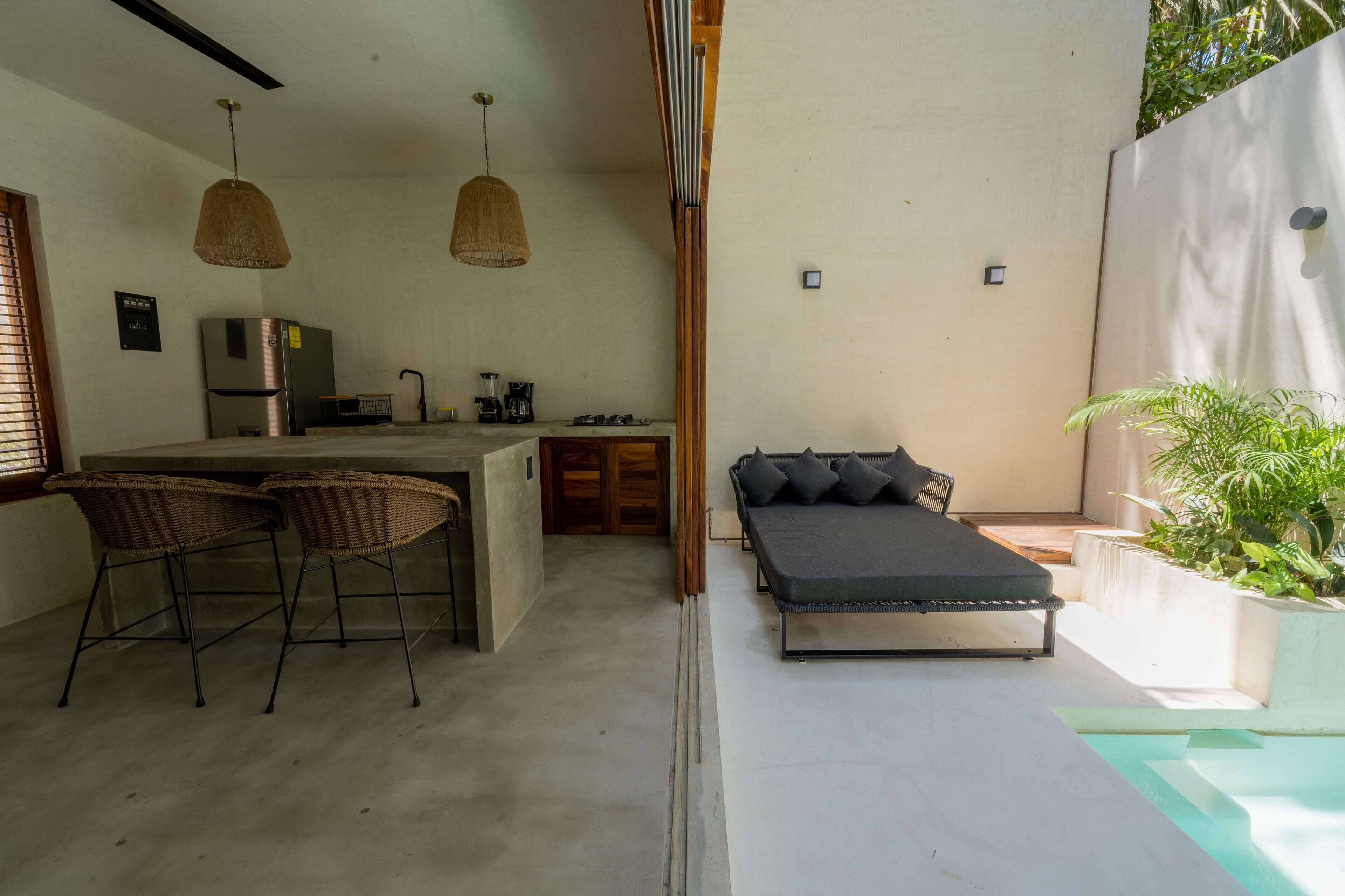 Cocina compacta con refrigerador, cafetera y comedor con dos sillas de mimbre.