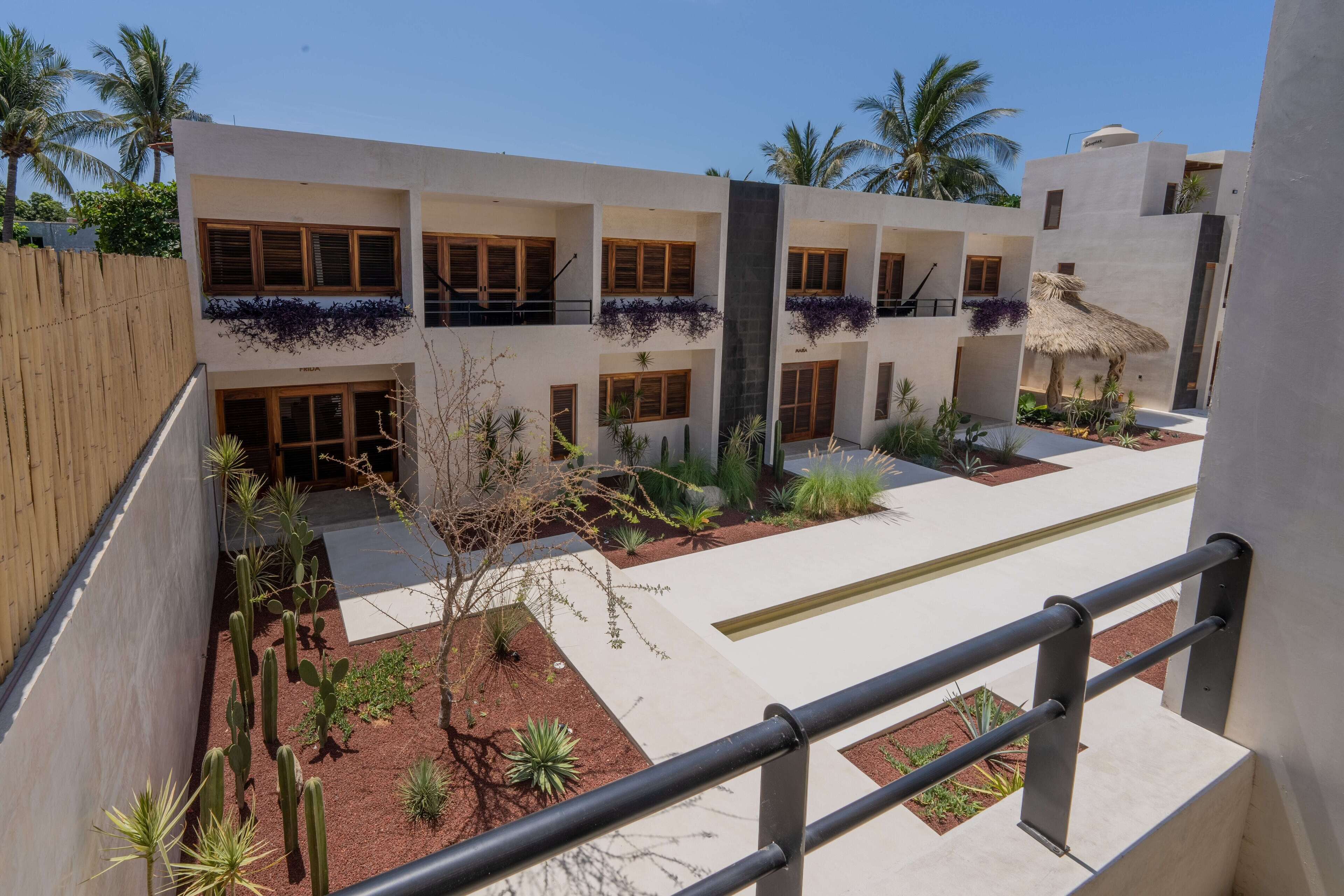 Un bâtiment moderne doté de nombreux balcons, une cour intérieure avec des cactus et une structure surmontée d’un toit de chaume.