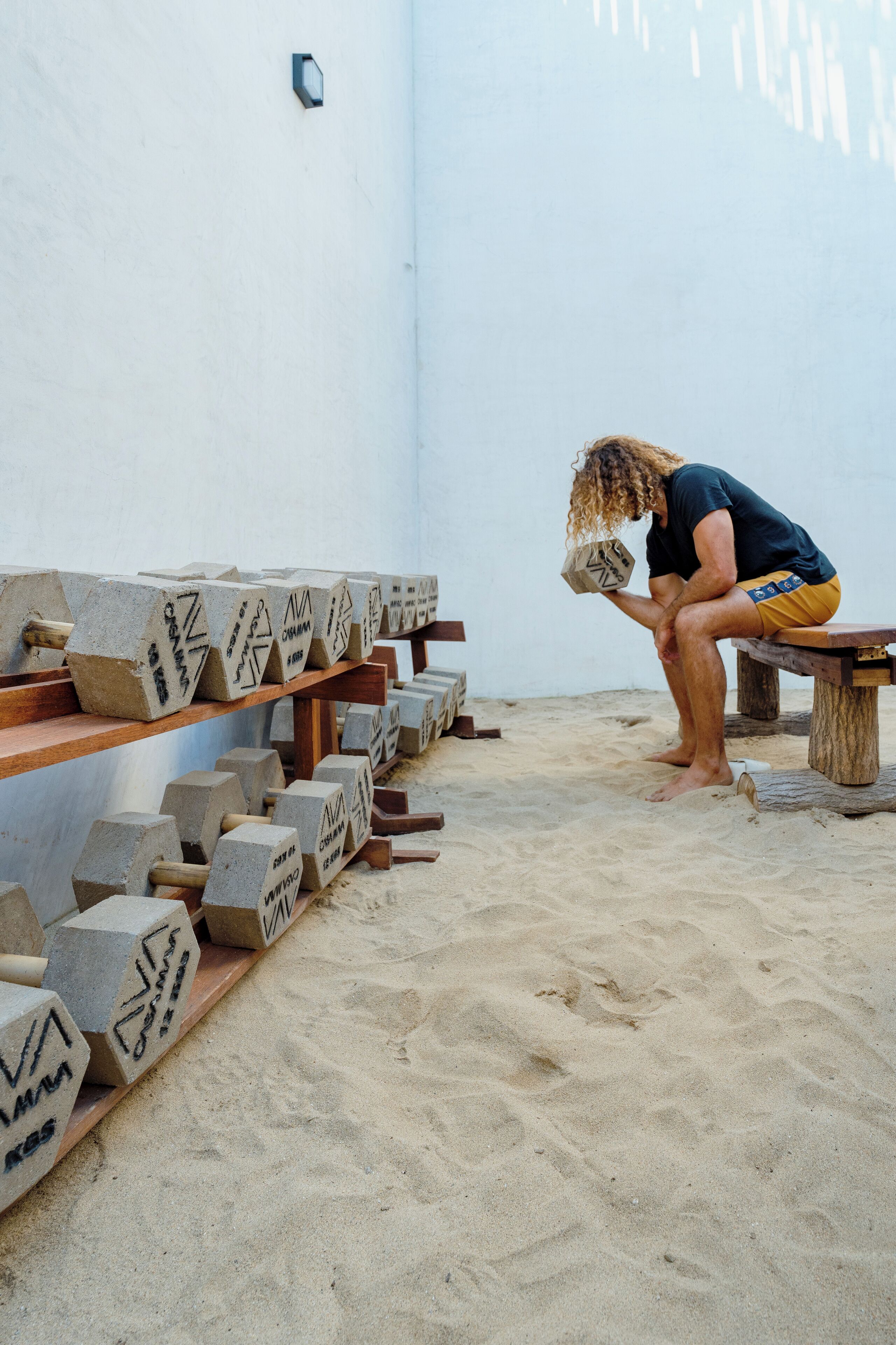 A person sitting on a bench in a room with a white wall and a wooden shelf holding several concrete blocks.