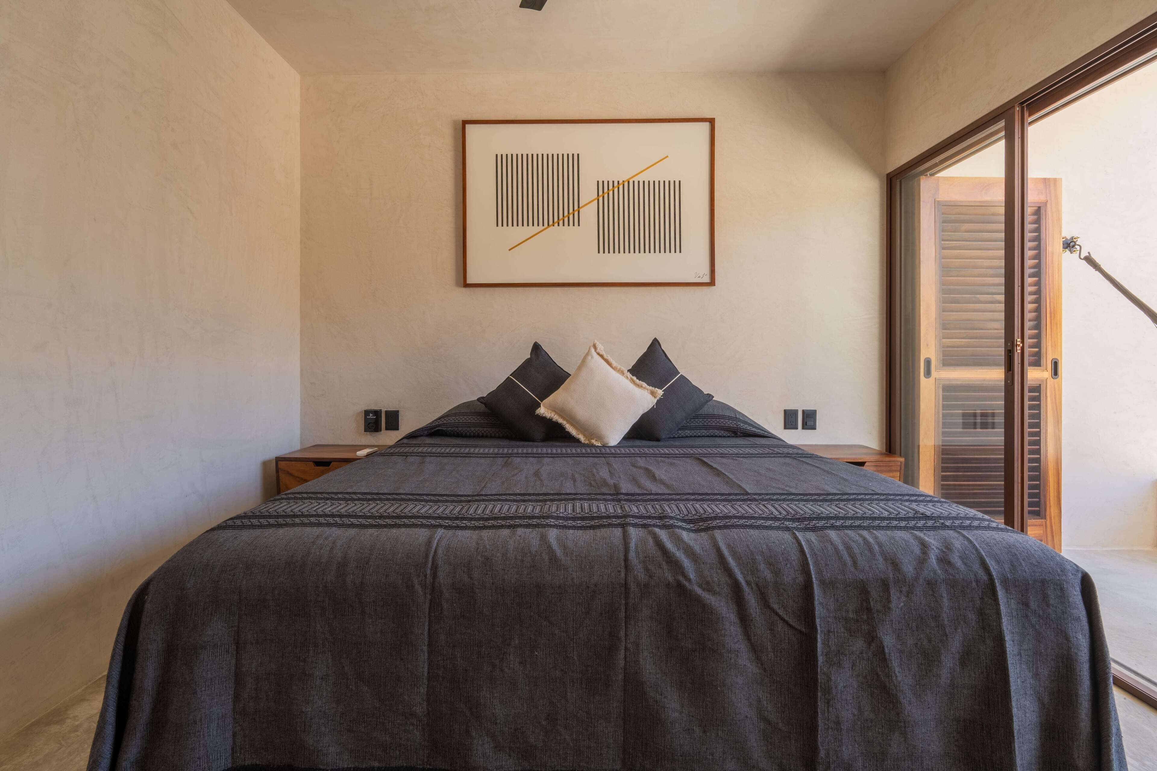 A bedroom with a large bed, a framed artwork on the wall, and a sliding door to the right.