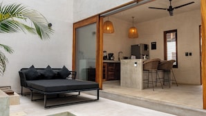 Un espacio exterior moderno con piscina, un sofá negro con cojines y un comedor con sillas de mimbre.