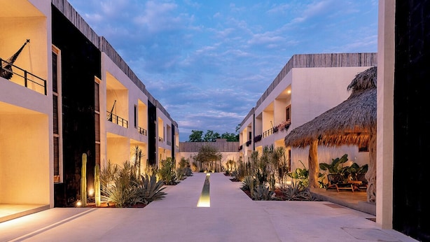 Un hotel moderno con un patio central, que presenta una estructura de techo de paja y una variedad de plantas.