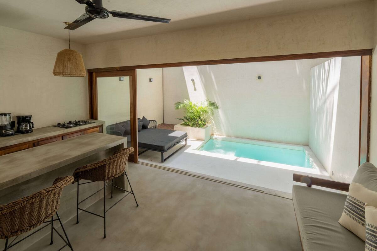 Une cuisine moderne avec un coin bar, un espace salon doté d’un canapé et de fauteuils, et une vue sur une piscine extérieure.