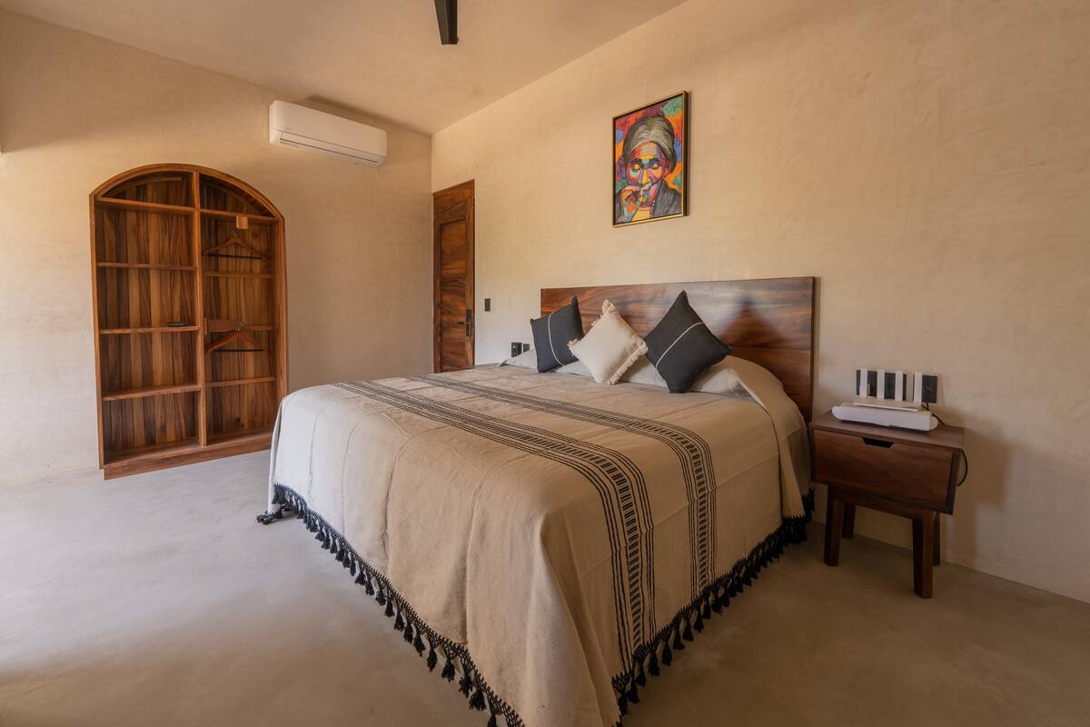 Une chambre à coucher avec un grand lit, une armoire en bois, une table de chevet et un tableau au mur.