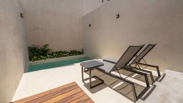 Un área de piscina moderna al aire libre con dos sillones de descanso, una mesita y una terraza de madera.
