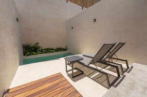 Un área de piscina moderna al aire libre con dos sillones de descanso, una mesita y una terraza de madera.