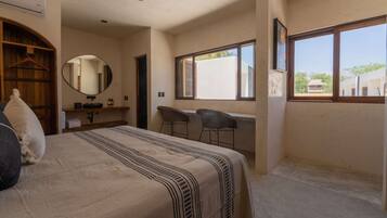 A bedroom with a bed, a desk, two chairs, a mirror, and a window.