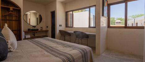 A bedroom with a bed, a desk, two chairs, a mirror, and a window.