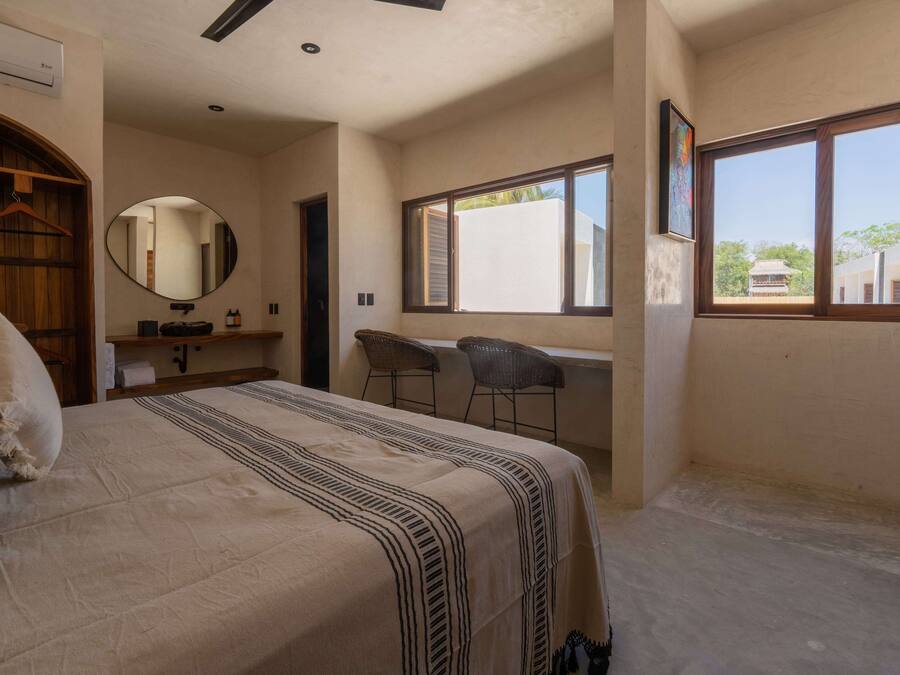 A bedroom with a bed, a desk, two chairs, a mirror, and a window.