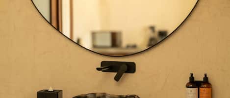 A bathroom with a round mirror, wooden countertop, sink, and two bottles of toiletries.