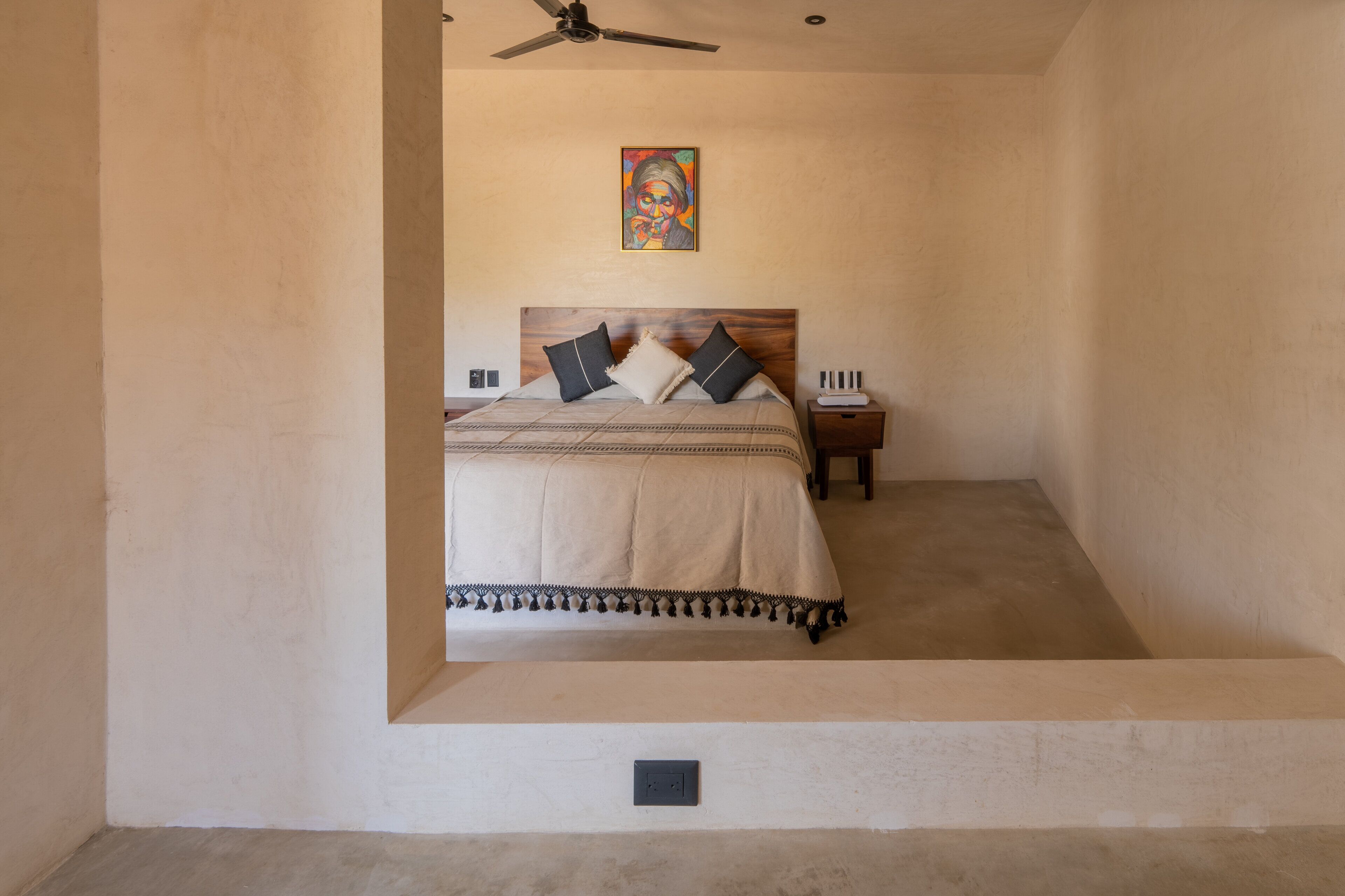 A bedroom with a bed, a nightstand, a ceiling fan, and a painting on the wall.