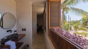 A bathroom with a wooden vanity, a round mirror, and a view of a beach with palm trees.