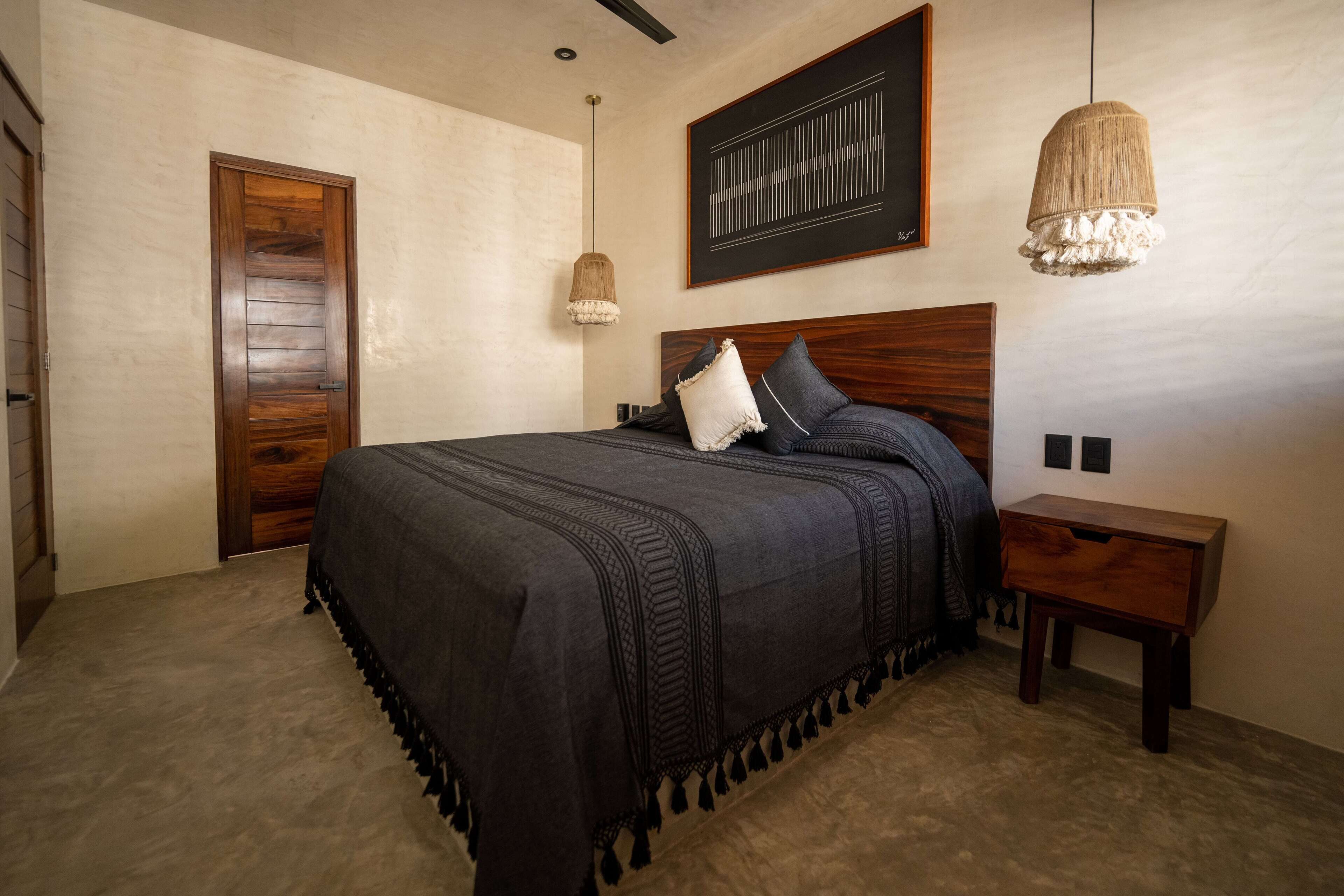 Un dormitorio con una cama grande, cabecera de madera, dos mesitas de noche, una lámpara colgante y una obra de arte enmarcada en la pared.