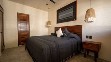 Un dormitorio con una cama grande, cabecera de madera, dos mesitas de noche, una lámpara colgante y una obra de arte enmarcada en la pared.