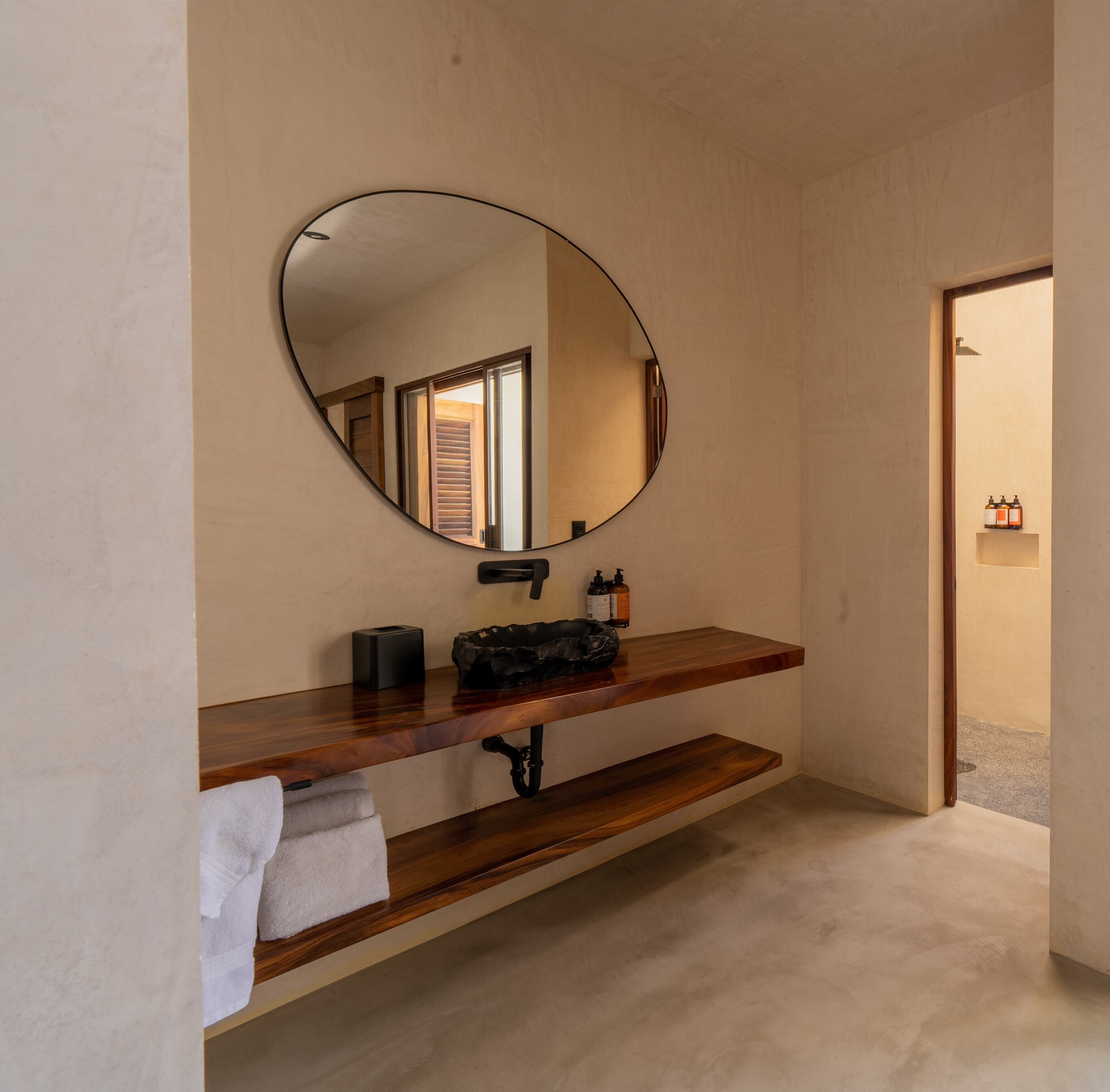 Een badkamer met een houten wastafelmeubel, een ronde spiegel en een handdoek op het aanrecht.