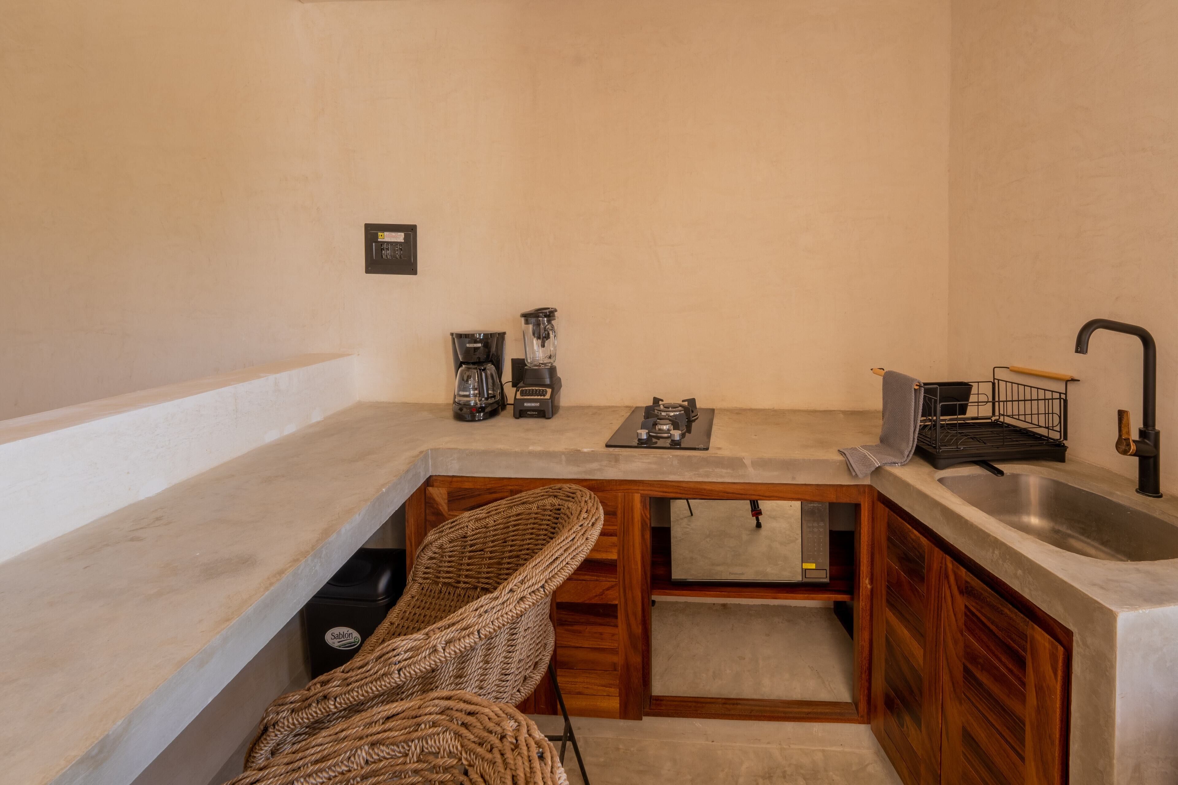 Una cocina compacta con un lavamanos integrado, armarios de madera y una silla de mimbre.