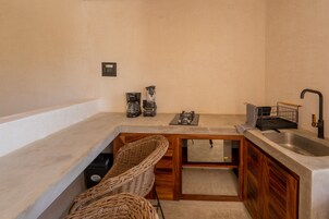 Una cocina compacta con un lavamanos integrado, armarios de madera y una silla de mimbre.