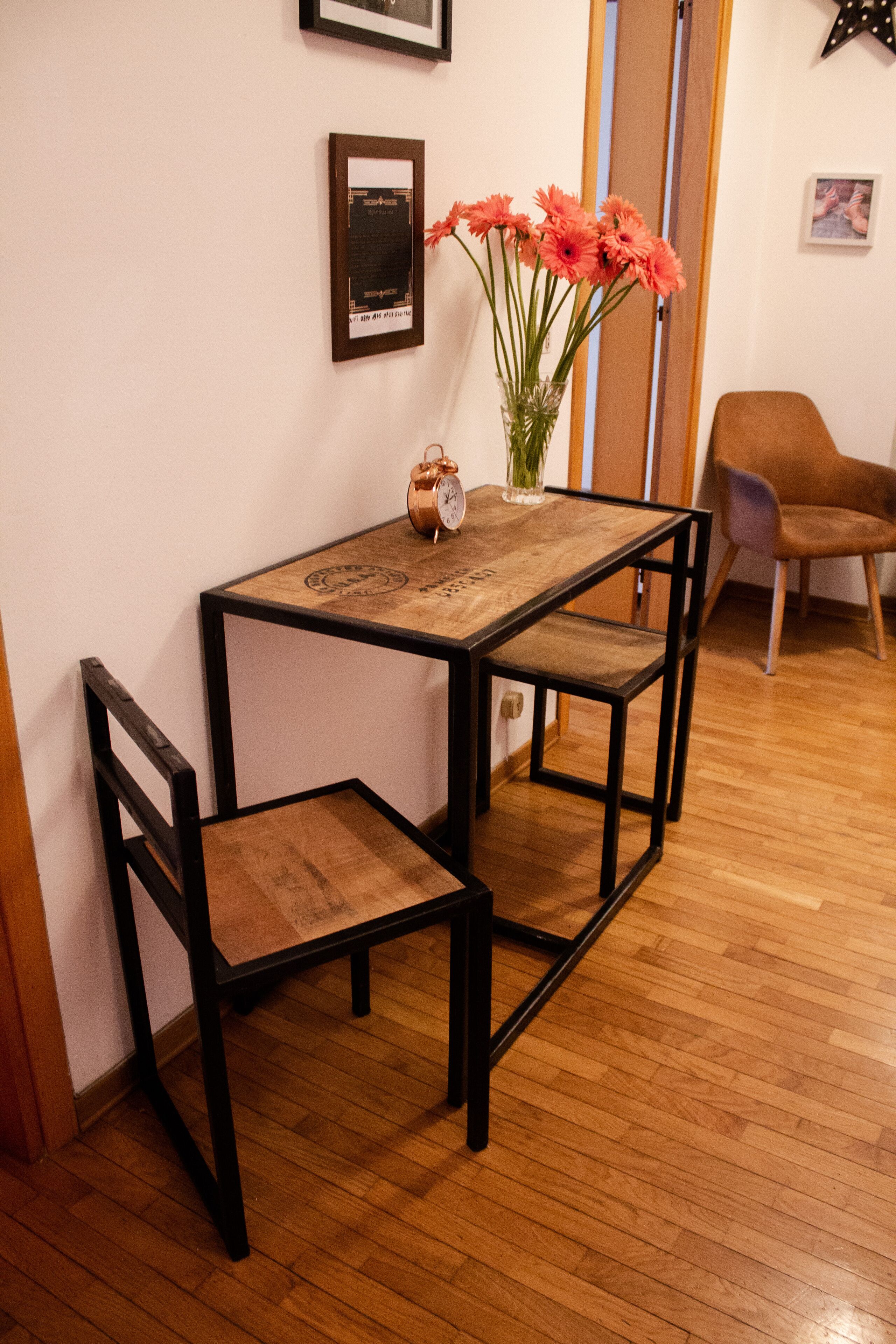 Ein kleiner Essbereich mit Holztisch und Stühlen, einer Vase mit Blumen und gerahmten Bildern an der Wand.