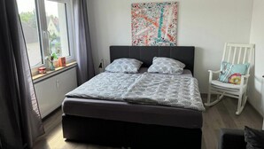 A bedroom with a bed, a window, a radiator, a chair, and a wall painting.