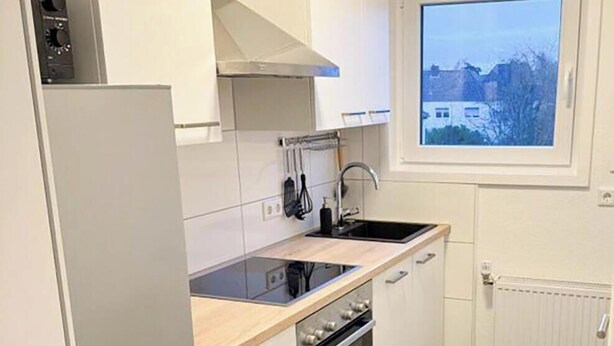 A compact kitchen with white cabinetry, a black oven, and a window with a view of buildings.