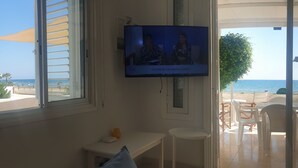 A living room with a television, a small table, and a view of the beach.