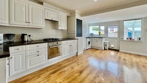 Ett rymligt kök med vita skåp, en spis i rostfritt stål och ett stort fönster som släpper in naturligt ljus.