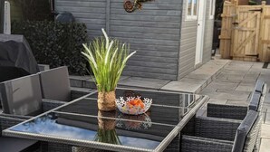 En uteplats med ett bord med glasskiva, möbler i rotting och en prydnadsväxt.