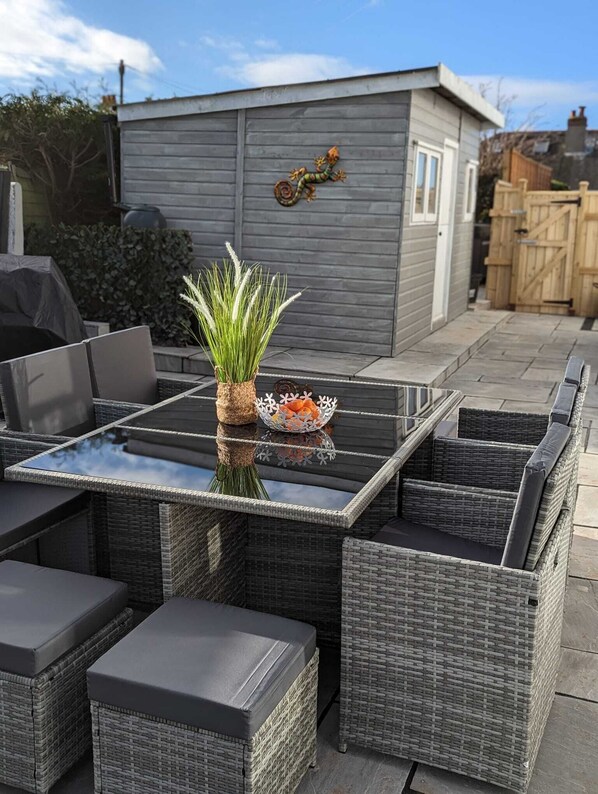 An outdoor patio with a glass-top table, wicker furniture, and a decorative plant. - Modern 3 bedroom house w/hot tub, garden and off street parking. Dog friendly. (Brixham)