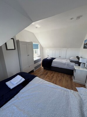 A bedroom with two beds, a wardrobe, a bedside table, and a window.