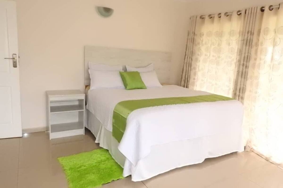 A neatly arranged bedroom with a bed, a bedside table, and a green rug.