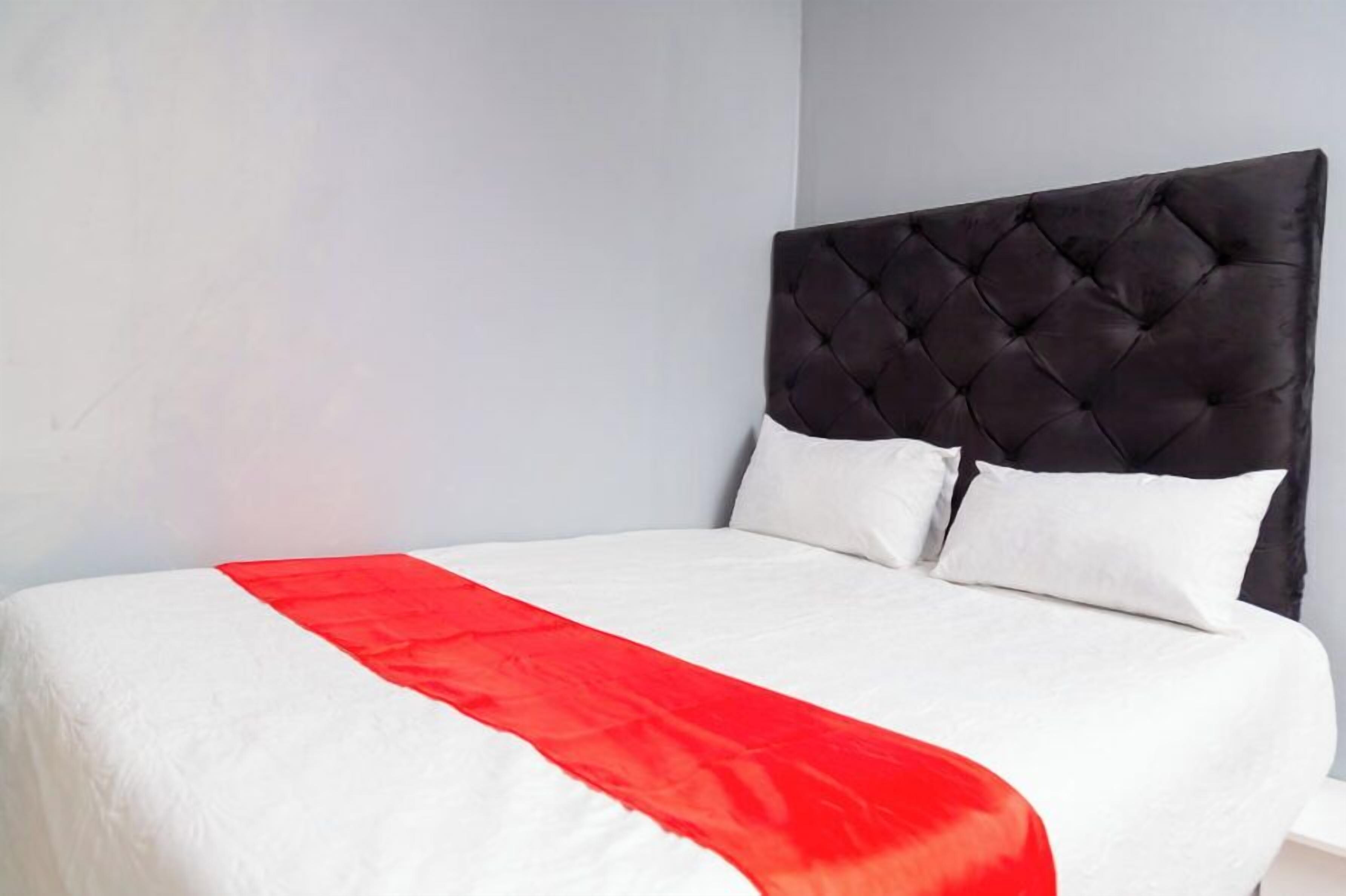 A bed with a tufted headboard, white bedding, and a red accent.
